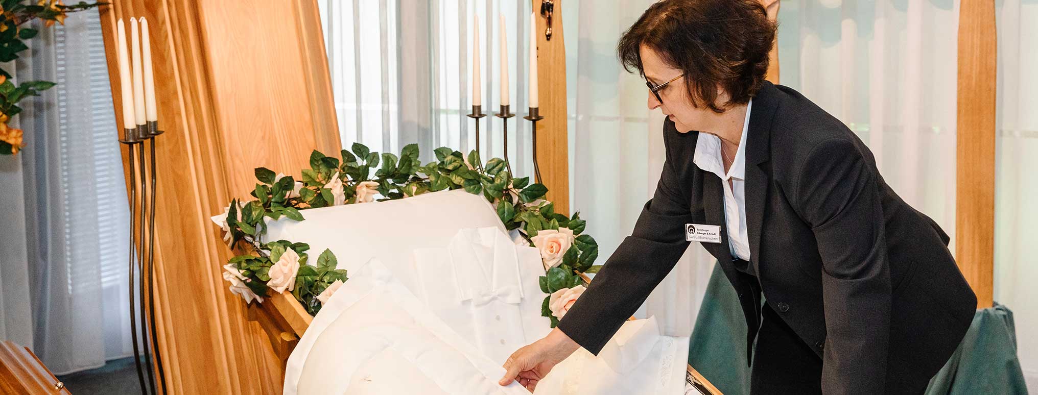 Bestatterin arrangiert ein weißes Totenhemd in einem offenen Sarg